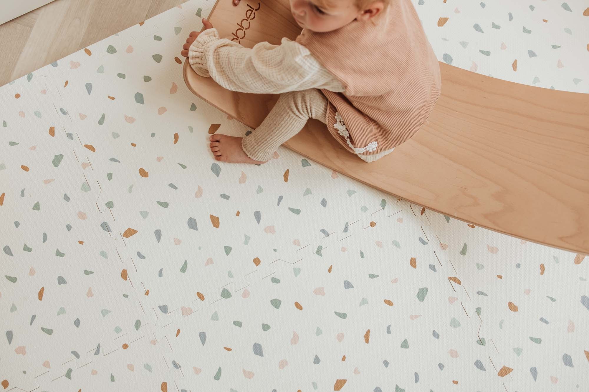 EEVAA village/terrazzo foam puzzle mat, child is sitting on a slide on top of the mat