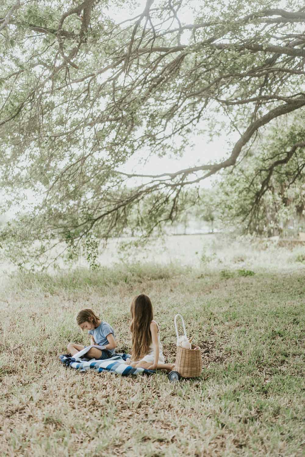 outdoor beach bag blue/green stripes, children sitting on open bag in garden under tree, reading a book and dreaming away                                                                             