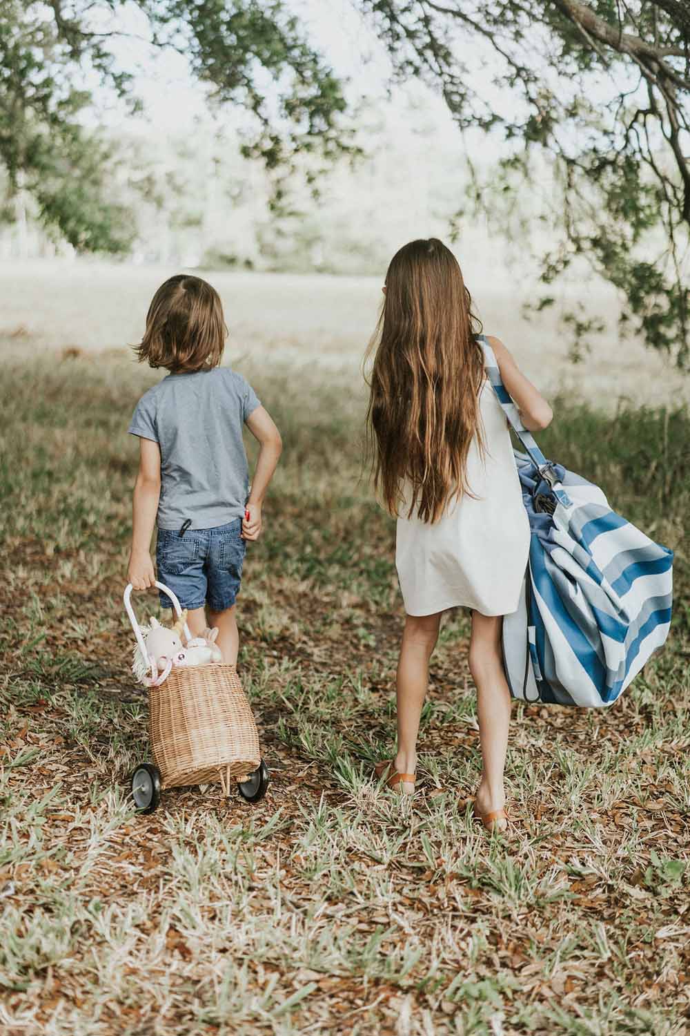 outdoor beach bag blue/green stripes, childres walking in a park under tree, child carrying the closed bag, other child carrying a wicker basket                                                                                                                                 