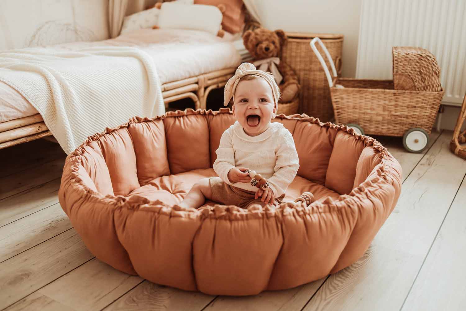 Bloom tawny brown organic babymat, raised edges, child sitting and playing on mat, kidsroom, bed and wicker baby carriage