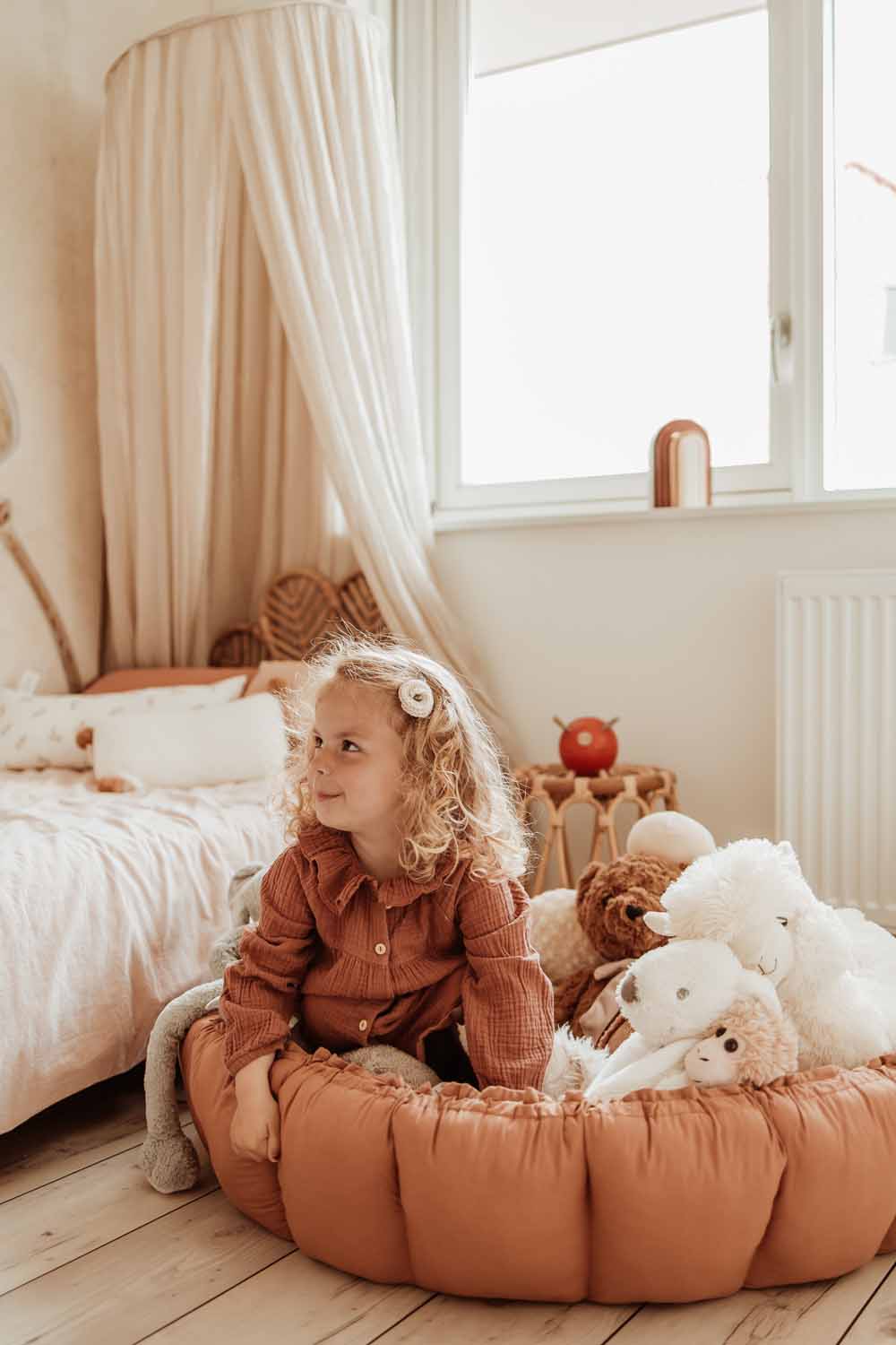 Bloom tawny brown organic babymat, raised edges, child sitting on mat between cuddles, next to bed in kidsroom