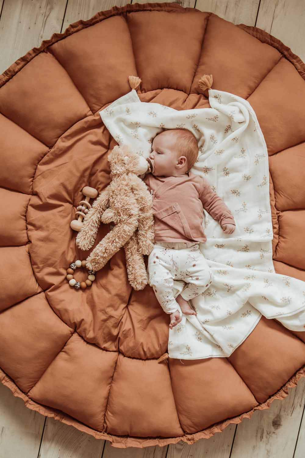 Bloom tawny brown organic babymat, little baby lying on mat on blanket, with cuddle bear in its arms