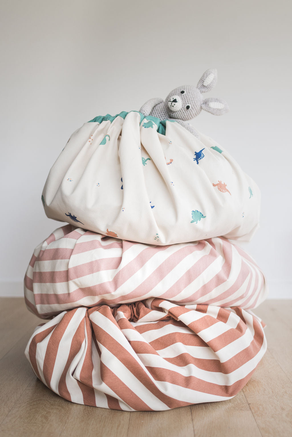 Brown Stripes toy storage bag, Stripes New Pink bag and Dino bag stacked on top of each other