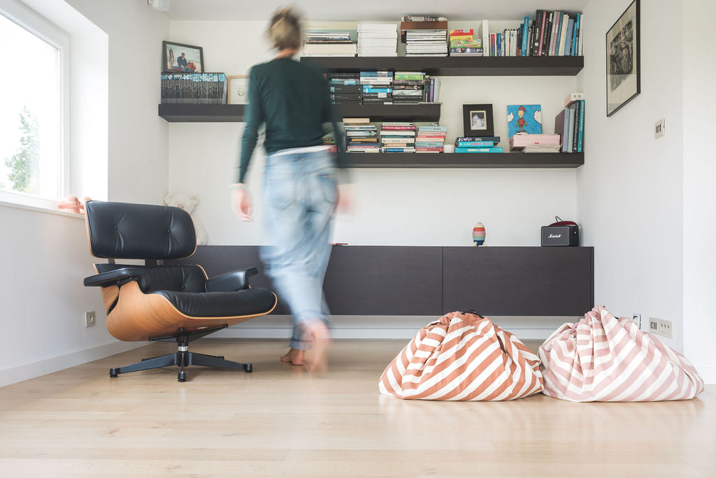 stripes pink new storage bag, lots of books, bag next to mustard striped storage bag, woman in livingroom