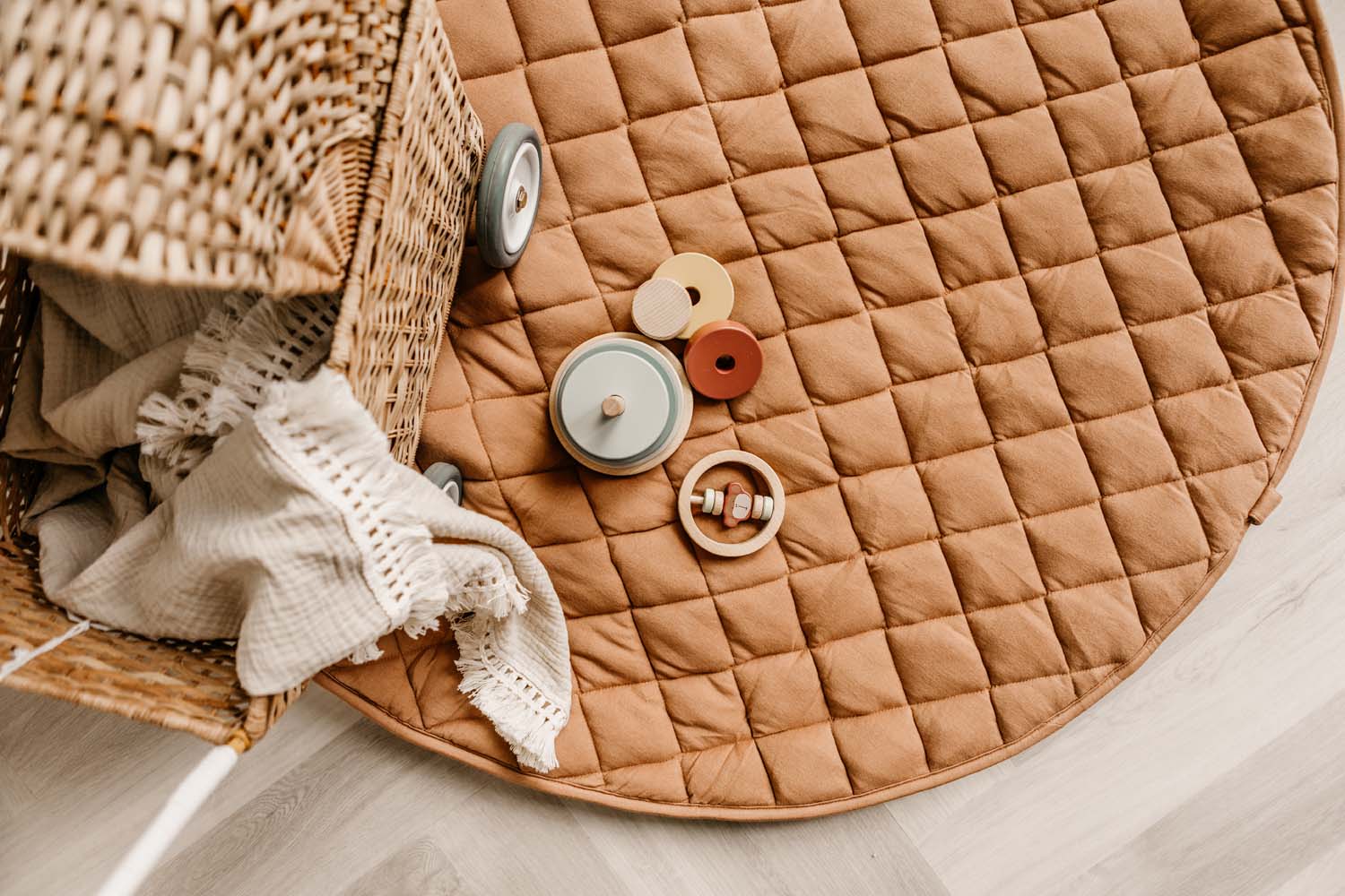 Tawny Brown soft padded baby play mat and storage bag, lying on floor, wooden toys, a wicker pram