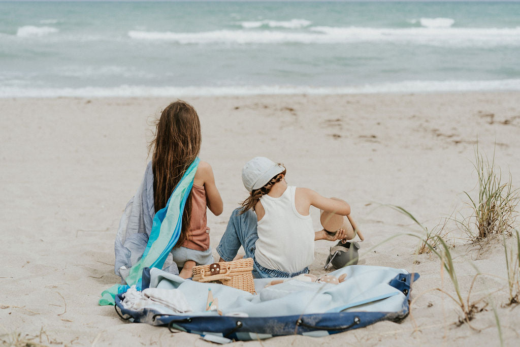 outdoor beach bag blue/green stripes, children sitting on the bag, looking at the sea while playing 