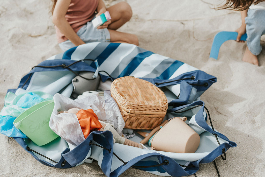 outdoor beach bag blue/green stripes, bag open on the beach, filled with lots of toys and a wicker picnic basket, children playing