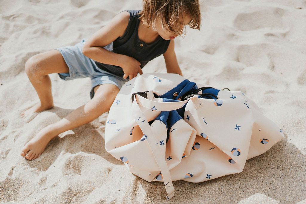 outdoor balloon storage bag and play mat, child looking in the bag while sitting in the sand, next to bag