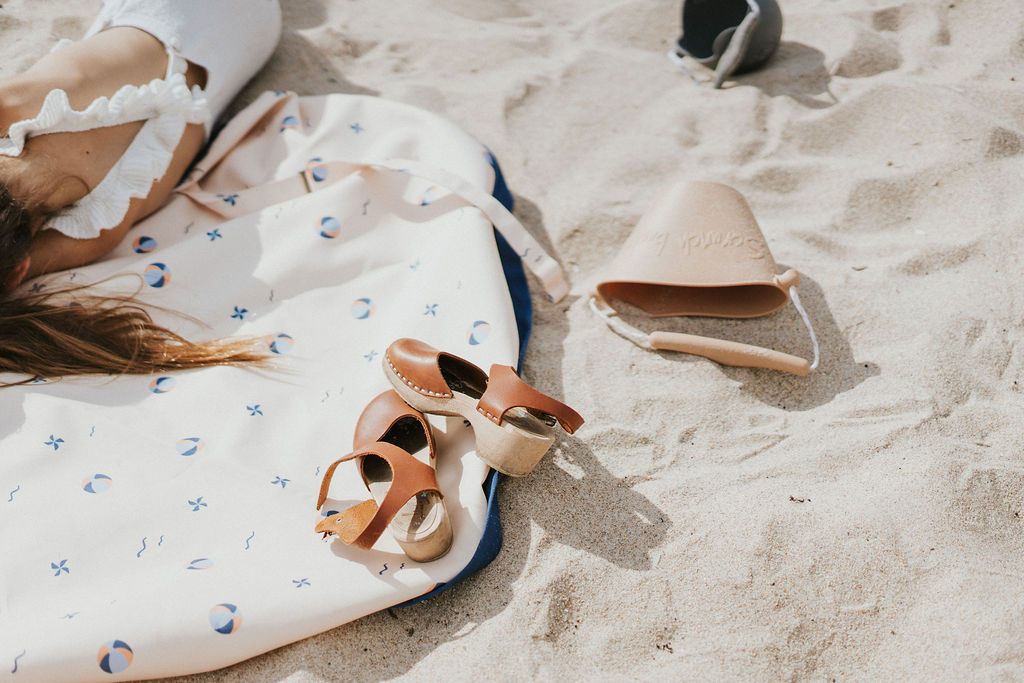 Play&Go outdoor storage bag and play mat, print balloon, bag in sand, child laying on the mat, beach toys and shoes of child