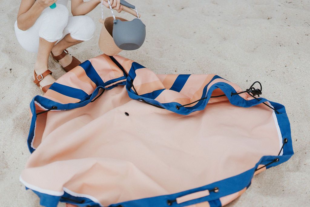 mokka stripes outdoor storage bag, open in the sand, child holding it's beach toys in it's hands