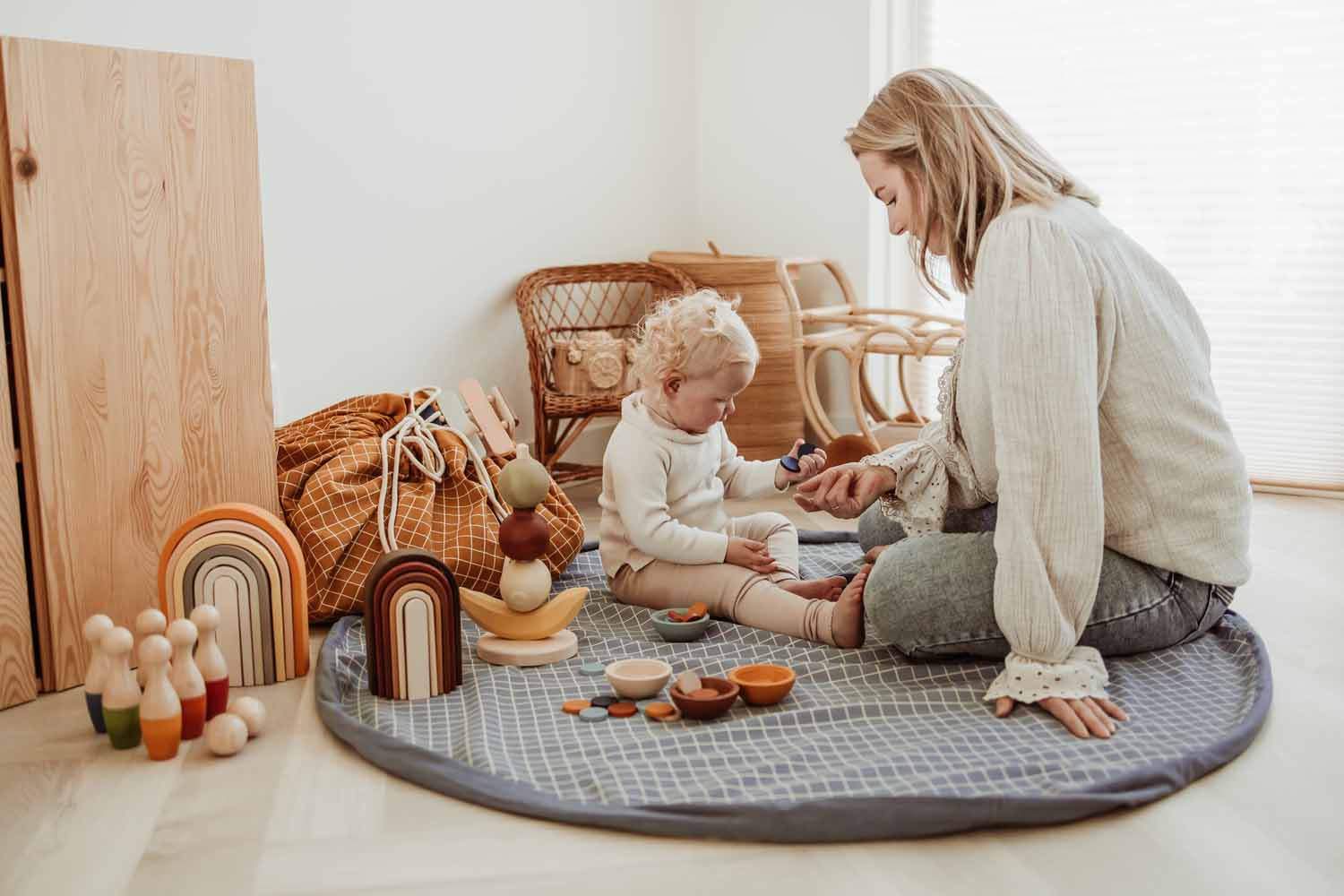 open organic storage bag grid blue, on floor in kidsroom, child and mom are playing on the mat with wooden toys, wicker chair, closed mustagrid mustard bag