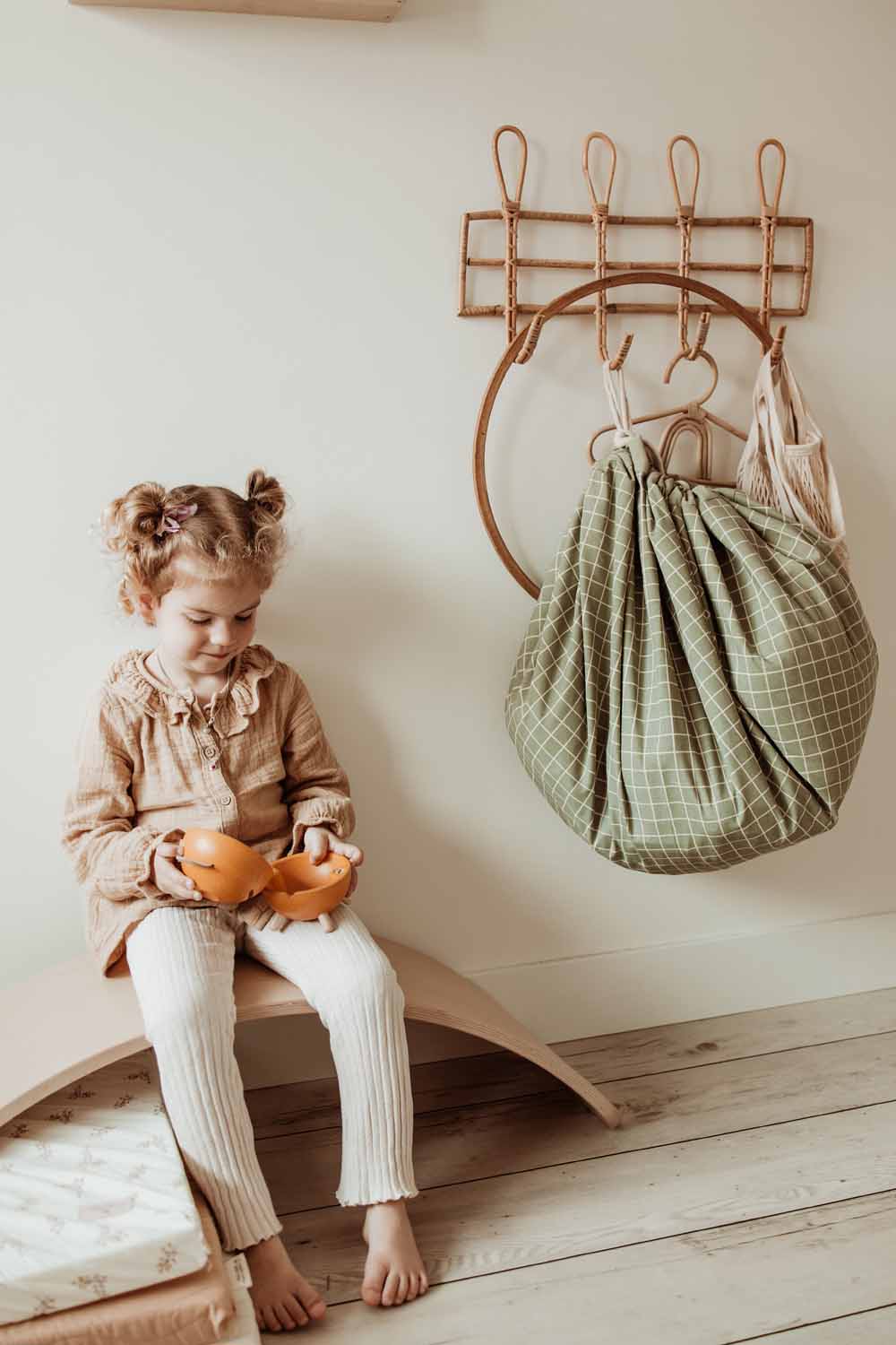 closed organic storage bag grid green, hanging on coat rack, child sitting on wooden bridge