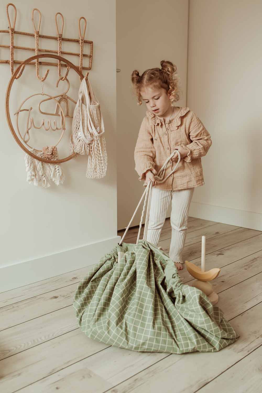 organic grid green storage bag, child pulling the rope to close the bag, coat rack on wall