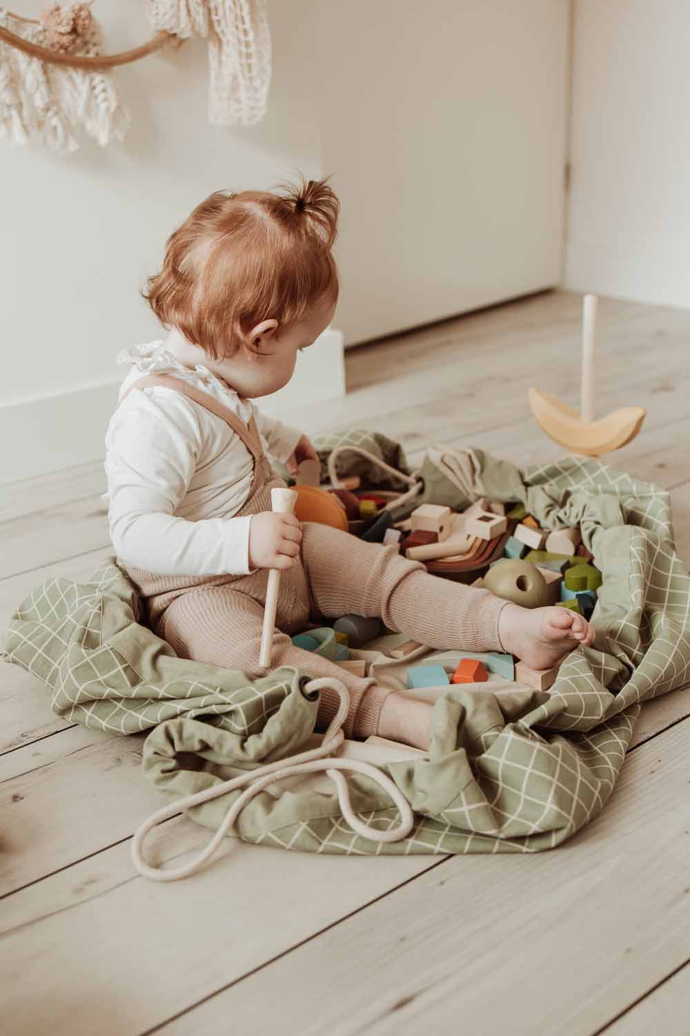 organic storage bag grid green, child sitting in the bag, filled with wooden toys