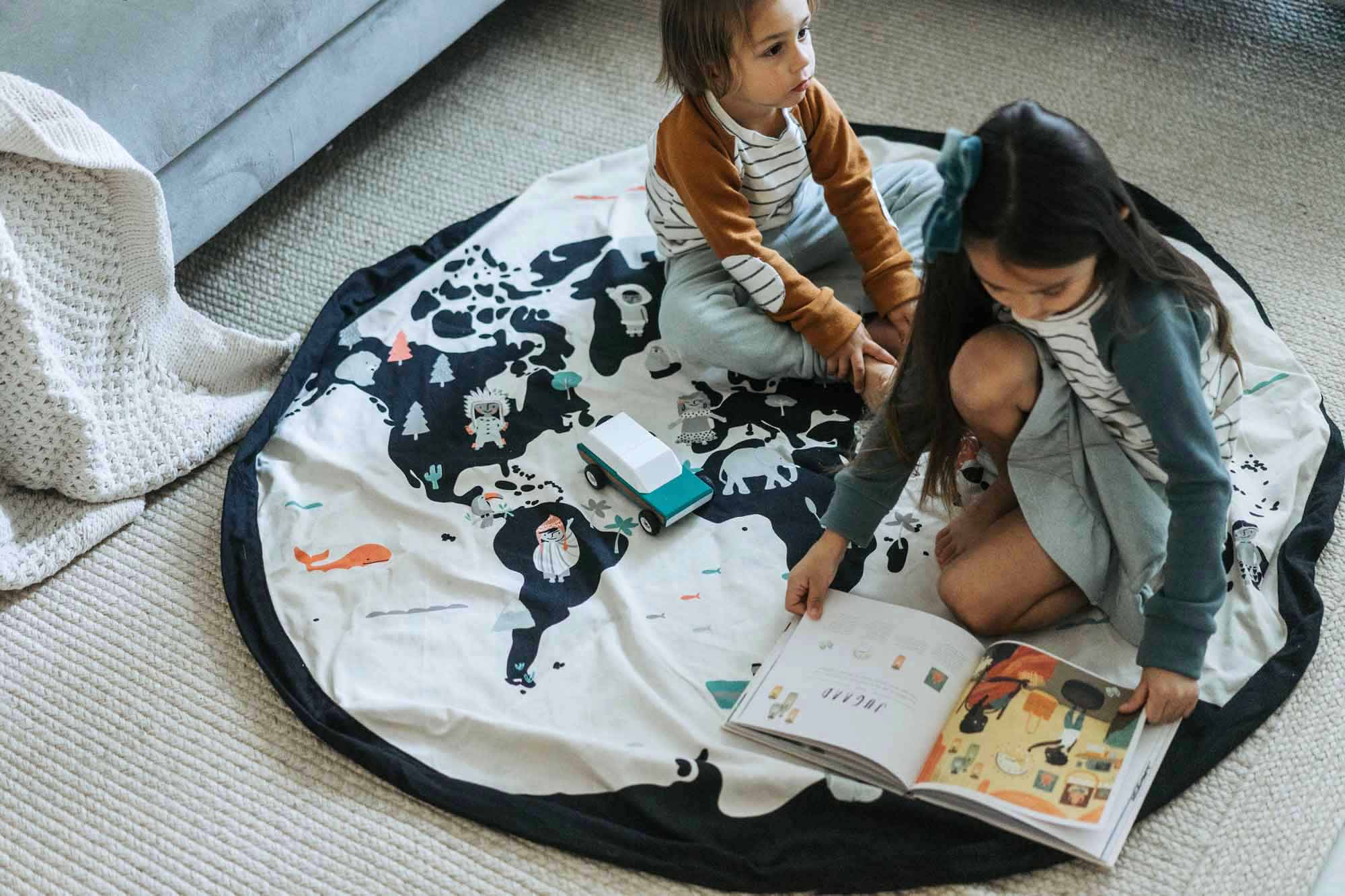 worldmap/stars storage bag, children sitting on the mat on carpet, child reading a book