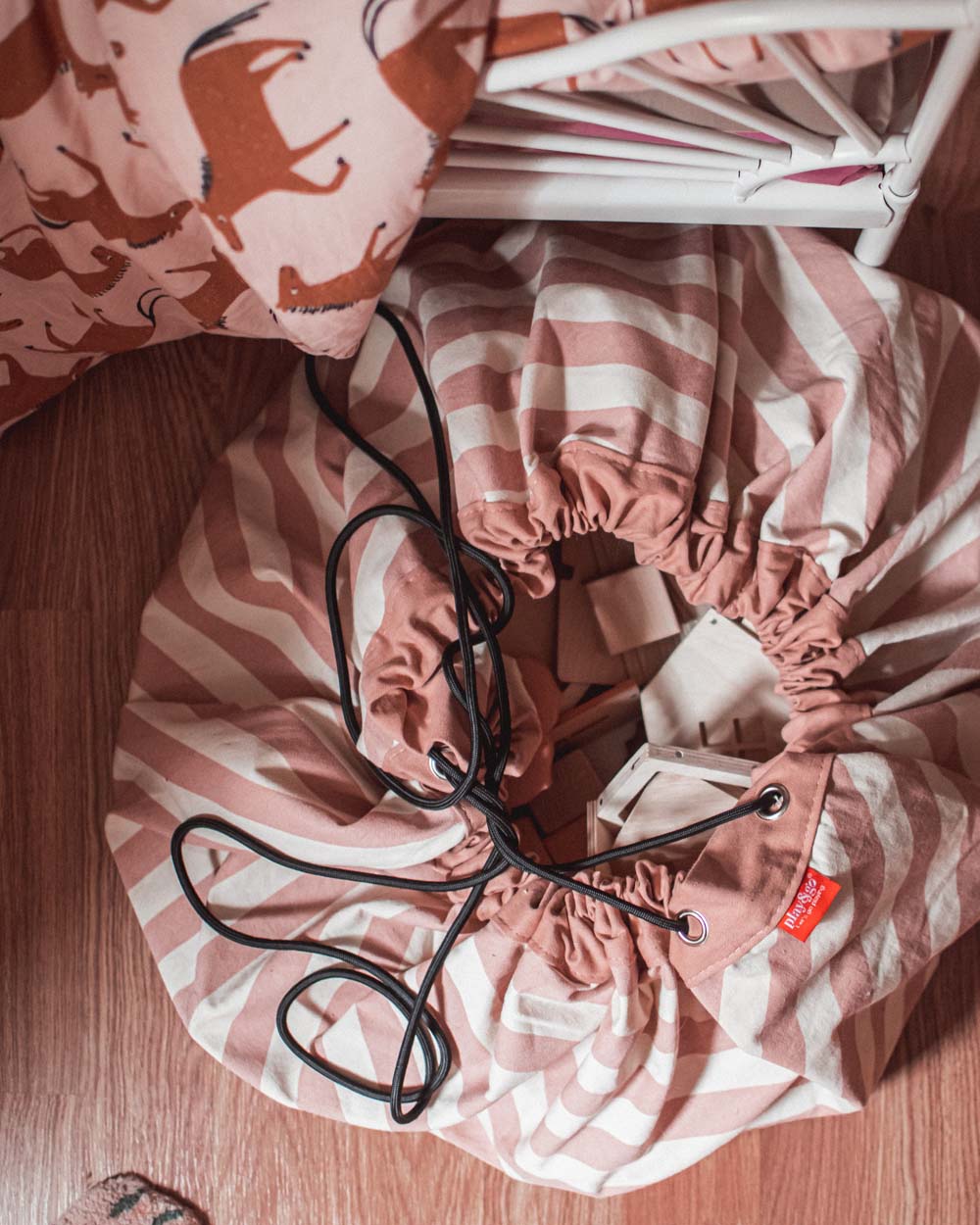 stripes pink new storage bag, filled with wooden toys, bag next to bed on floor