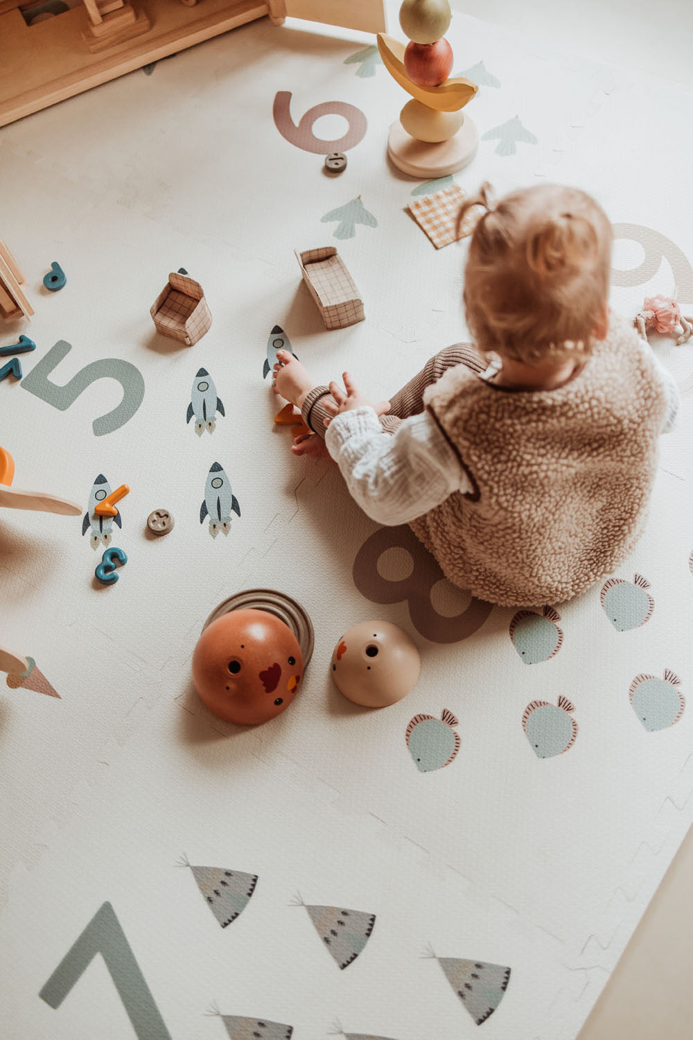 child sitting on numbers puzzlemat, playing with wooden toys