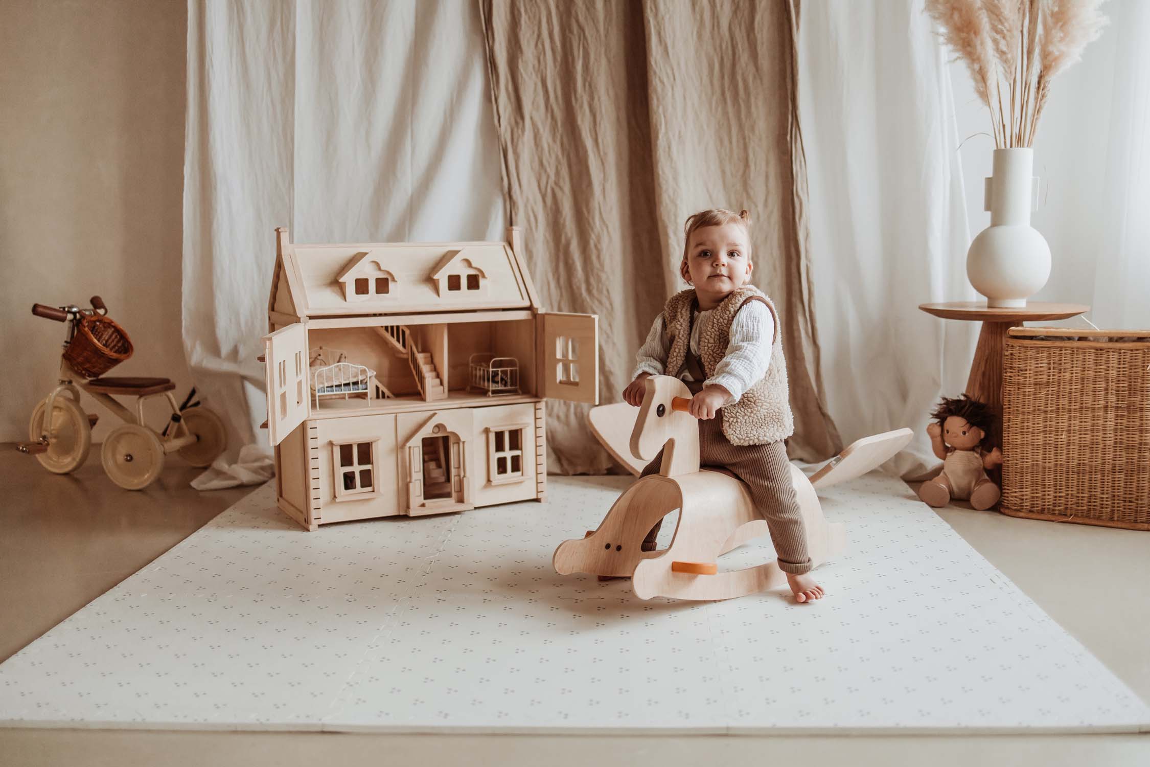 child sitting on rocking horse on dots puzzlemat in kidsroom, victorian play house and tricycle
