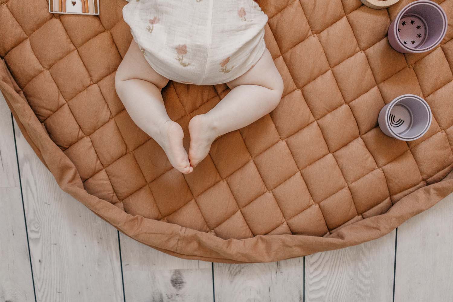 Tawny Brown quilted baby play mat and storage bag, little baby feet, baby lying between toys
