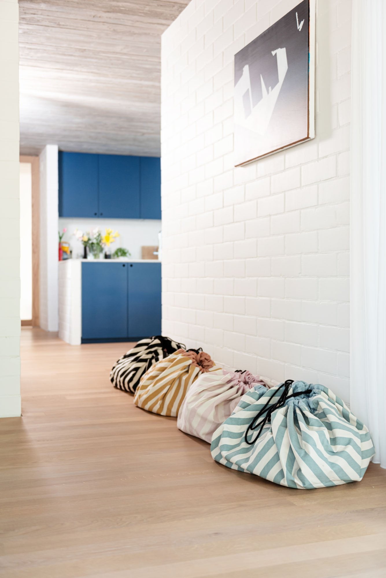toy storage bag and play mat, cool black, mustard, pink and green stripes, different bags against white wall